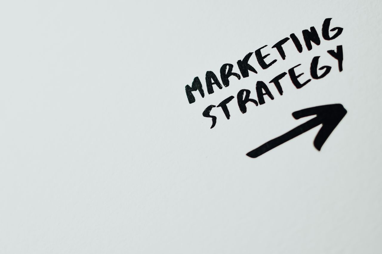 our-story Close-up of handwritten Marketing Strategy text with an arrow on white background.